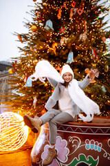 Smiling woman in winter style clothes posing at festive street market.  Young woman enjoying winter moments. Festive Christmas fair, winter holidays concept.