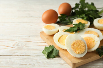 Board with boiled eggs on white wooden background