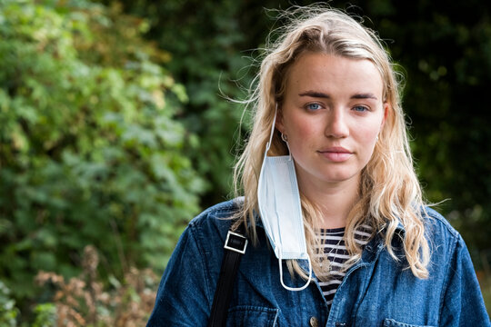 Portrait of young blond woman with her face mask dangling from one ear.