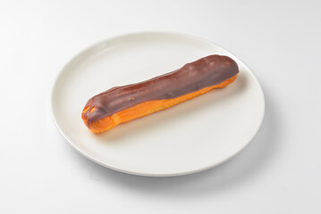 Milk chocolate eclair on plate on white background. Delicious vanilla dessert for tea time.