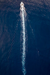 Aerial view of a boat sailing over blue water and leaving a trail of white bubbles
