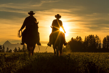 Two cowboys riding into the sunset across grassland with moutains behind, British Colombia, Canada.