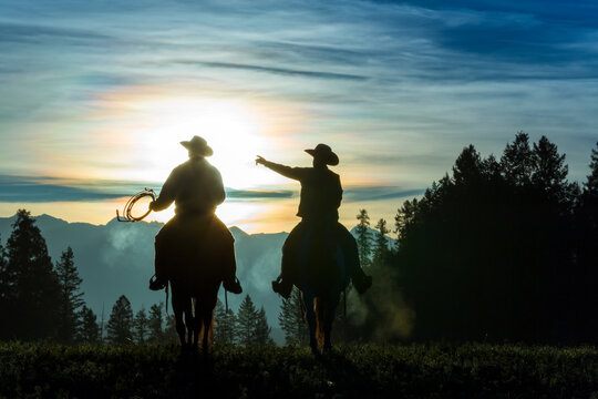 Two cowboys riding across grassland in early morning