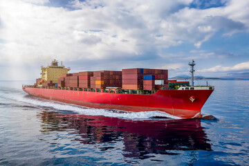 A red cargo ship loaded with many containers traveling over calm ocean