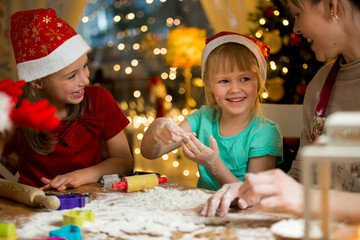Mother and little kids in red hats cooking gingerbread cookies and playing. Beautiful living room...