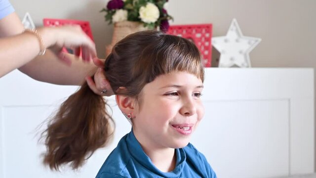 Mom combing her daughter's hair in the room on the bed. Little happy girl at home in the bedroom. High quality 4k footage