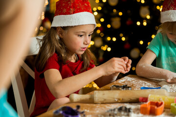 Mother and little kids in red hats cooking gingerbread cookies and playing. Beautiful living room...