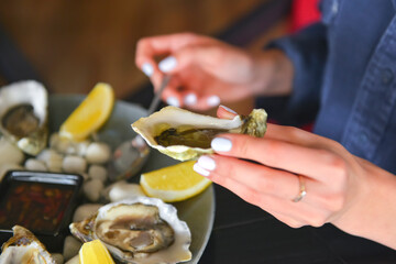 Fresh oysters as well as fine dining, young attractive woman eating oysters in restaurant.