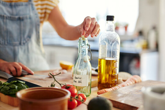 Woman putting garlic into bottle of olive oil in kitchen