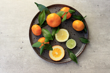 Plate with citrus fresh fruit tangerines with leaves, lemon, lime orange on a dark round plate on a concrete background . vitamins, close-up