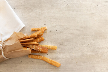 grissini breadsticks with sesame seeds in a paper bag with a bow on a light background with a checkered towel with space for text top view