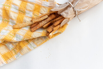 grissini breadsticks with sesame seeds in a paper bag with a bow on a light background with a checkered towel with space for text top view