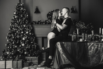 Passionate romantic couple spend time together before the New Year near a beautiful Christmas tree at home. Sexy young woman and handsome man hugging and celebrating new year