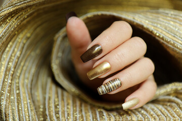 Fashionable manicure with a matte Golden color of nail Polish and brown on a long nail shape.