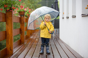 Cute blond toddler child, boy, playing in the rain with umbrella on a foggy autumn day