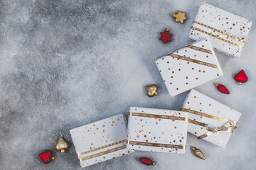 Gift boxes in white paper with stars and dots with golden ribbons on grey background. Flat lay with copy space. Christmas and New Year background. 