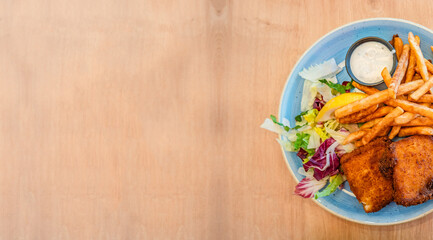 Banner with delicious and appetizing fish and chips with sauce and salad and fork and knife at wooden background for copy space text, details, closeup.