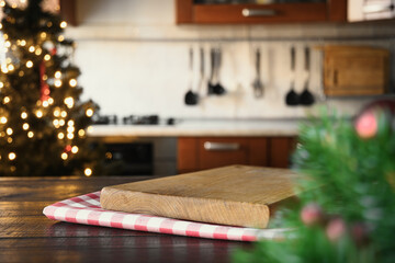 Wooden tabletop with cutting board and blurred modern kitchen with Christmas tree.