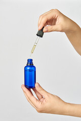 Naklejka premium Female's hand holds a pipet of natural extract CBD oil against a light grey background.