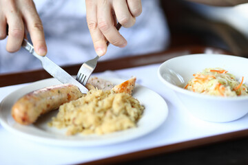Dinner dish of stewed cabbage and salad sausages is on table visitor holds fork and knife in his hands. Cooking recipes concept