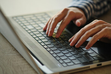 Close-up of female hands typing on the keyboard work process, checkered shirt.