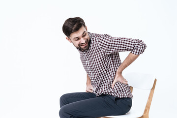 A man sits on a chair and grabbed for a sore back.