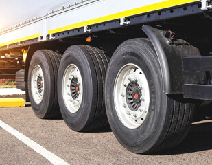 Fototapeta na wymiar Wheels with rubber on the cargo 3-axle trailer of the tractor. The concept of choosing high-quality rubber for road transport. Fuel economy and road safety