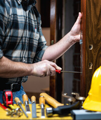 Close-up. Carpenter with screwdriver fixes the lock of a wooden door. Construction industry. 