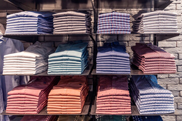 Clothes displayed in store, men's shirts shirts of different colors on the shelf, beautifully and neatly arranged in piles