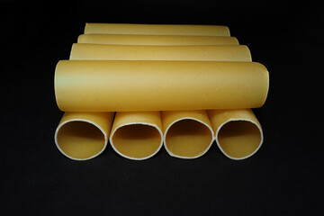 eight tubes of raw cannelloni on a black background front view . before cooking in Italian cuisine