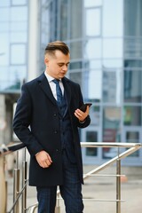 Handsome businessman standing by office building having business call on mobile phone