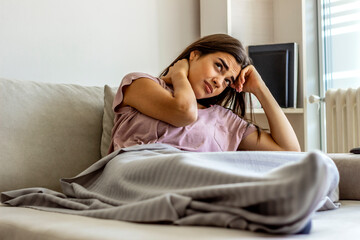 Young woman experiencing neck pain at home. Photo of woman sitting in bed and suffering from neck ache at home. Cropped shot of an attractive young girl suffering from neck ache while sitting at home.