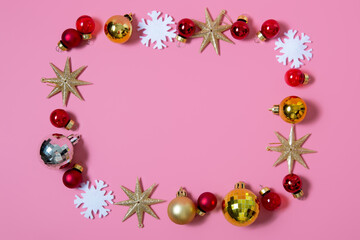 Frame made of red and gold christmas balls, gold stars and snowflakes on a pink background. christmas celebration concept. flat lay, copy space, top view, border.