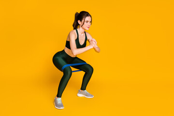 Fototapeta na wymiar Young lady house gym training stretch resistance stripe doing squats wear sports suit isolated yellow color background