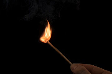 Hand holding a lighted match with fire flame and smoke on a black background.