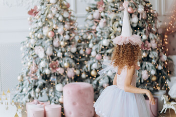 Beautiful Christmas decor in pink in the children's room. Girl playing near the Christmas tree - 391482588