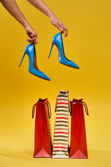 .Female hands holding shoes on a yellow background, shopping bags are standing nearby