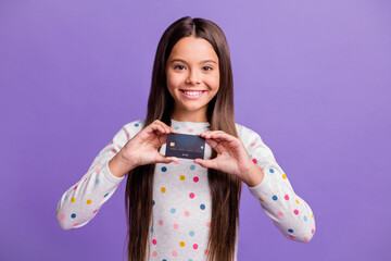 Photo portrait of cheerful schoolgirl showing plastic bank credit card isolated on bright violet color background