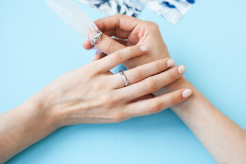 beautiful manicured woman hands with white feather on blue background
