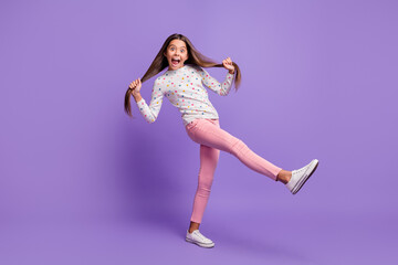 Full length body size photo of silly playful small girl grimacing keeping long hair tails kicking isolated on bright purple color background