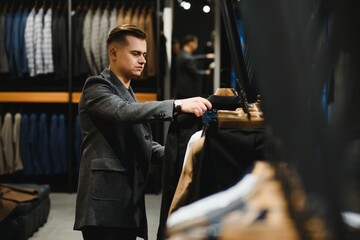 client handsome young businessman in a costume shop inspects the material of the sleeve of the jacket on the hanger.