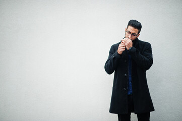 Middle eastern entrepreneur wear black coat and blue shirt, eyeglasses standing against white wall...