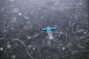 a man in ice skates lies on the transparent ice of the lake, view from above, aerial photography