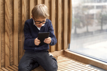 boy with glasses plays online games on the tablet by the window