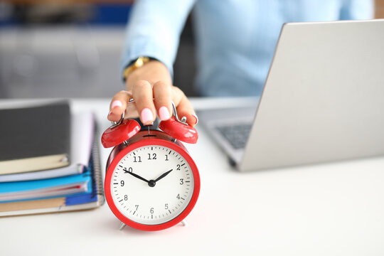 Woman's Hand Lies On Red Alarm Clock Notebooks And Laptop Lie Next To It. How To Deal With Stress When There Is Deadline Concept At Work