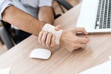 A male injured hand lies on table at a computer.