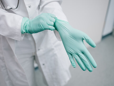 Junge &Auml;rztin zieht sich vor der Behandlung Handschuhe an