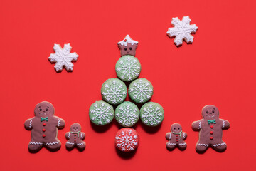 Gingerbread family standing by a Christmas tree made of macarons with a gingerbread star topper and snowflake cookies falling on a red background