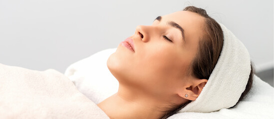 Side view of young woman lying on beautician table with closed eyes while waiting for cosmetic...