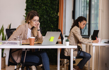 Fototapeta premium Portrait of a young female businesswoman working in an office while sitting at a table with colleagues in the background.